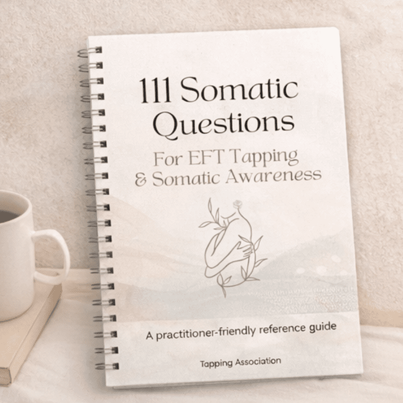 A spiral-bound "111 Somatic Questions for EFT Tapping – Practitioner Reference Guide (Printable PDF)" rests on a light surface beside a cup.